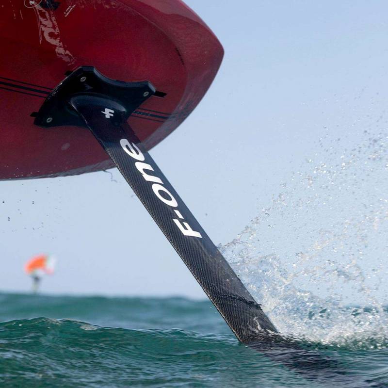 Mât Carbon HM 14 en action sur une mer calme, rider flou en arrière-plan, idéal pour le wingfoil et le foil de haute performance.