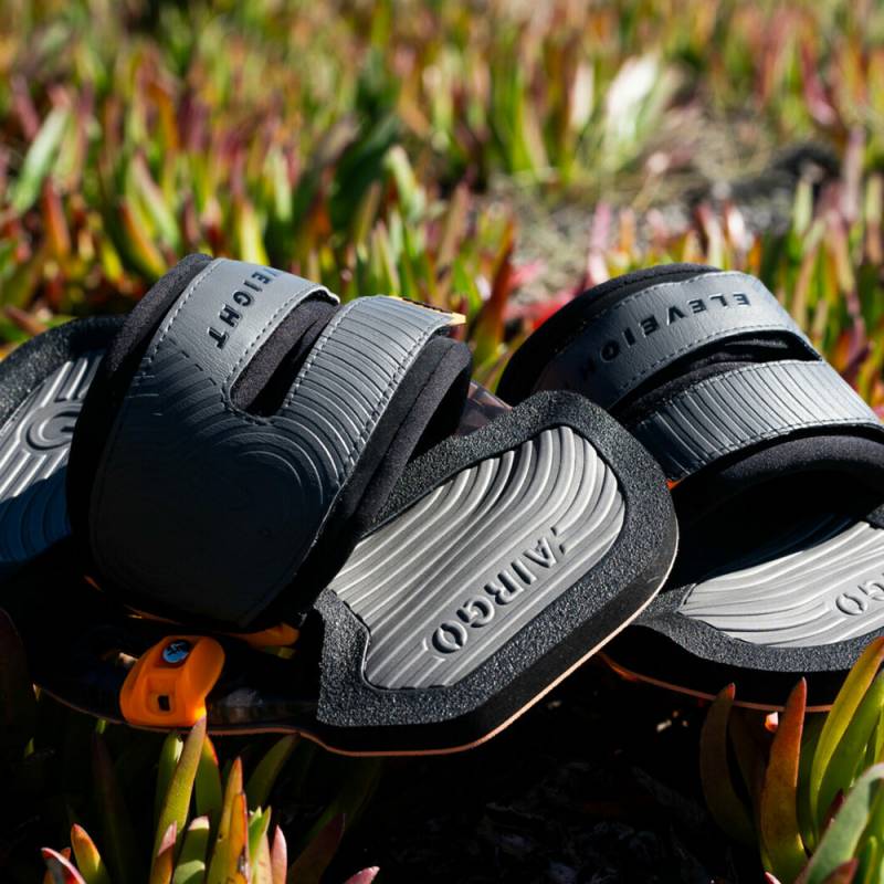 Gros plan des pads Eleveight Airgo V4 pour le kitesurf, posés sur des plantes vertes, avec des extrémités rouges.