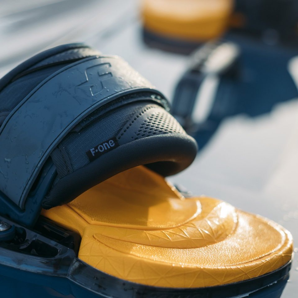 Gros plan sur un Pad F-ONE Platinium 3 de couleur jaune et noire, mettant en évidence le logo F-ONE et les détails du strap nouvelle génération en gel foam et néoprène résistant. Cette image illustre la construction robuste et les textures antidérapantes du pad, essentielles pour un grip total et une durabilité exceptionnelle en kitesurf.