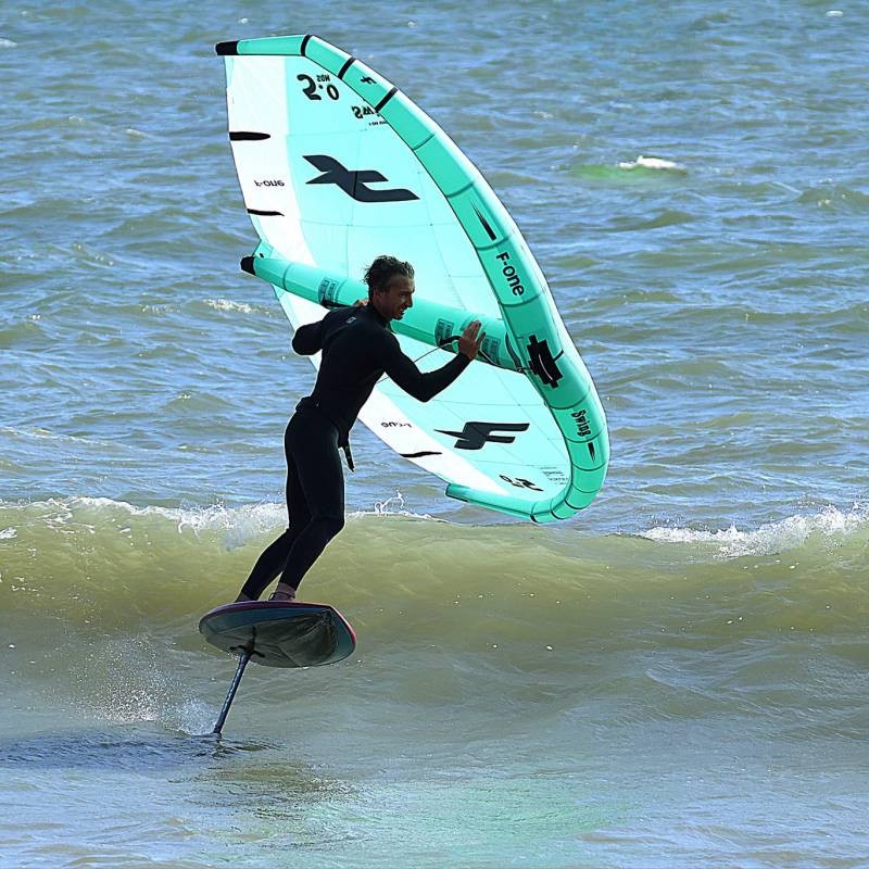 Rider en action de wingfoil sur mer calme avec le mât F-One Carbone 16 monté sur sa planche – stabilité et performance en navigation.