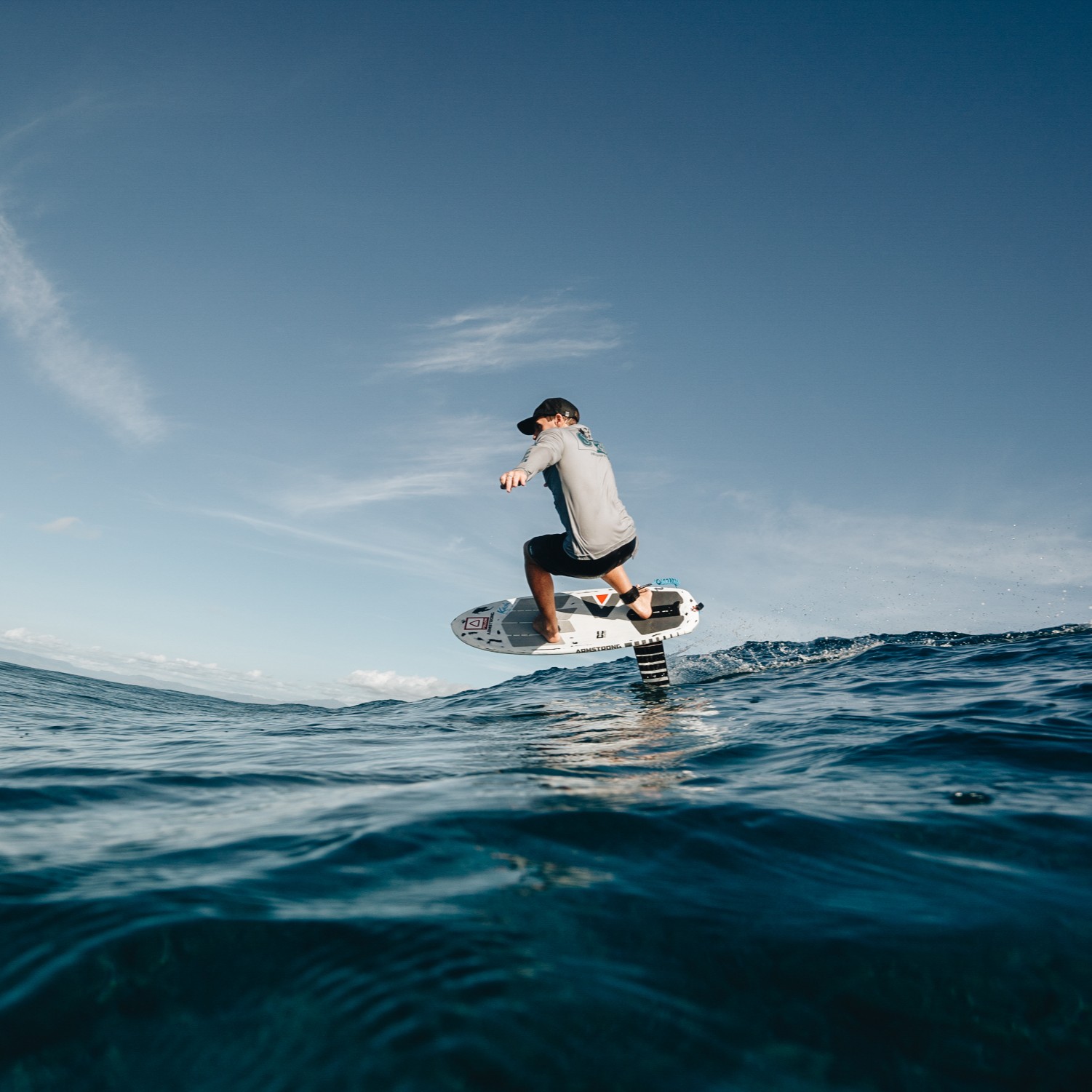 Surfeur sur une planche de foil, pratiquant le foil dans une mer calme sous un ciel dégagé, avec un mouvement fluide et un léger rebond des vagues