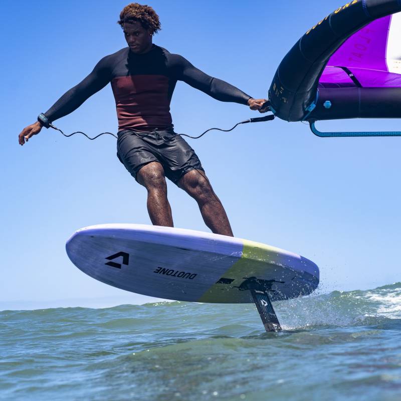 Rider en wingfoil avec planche à foil Duotone violette et jaune, évoluant au-dessus de l'eau par temps ensoleillé