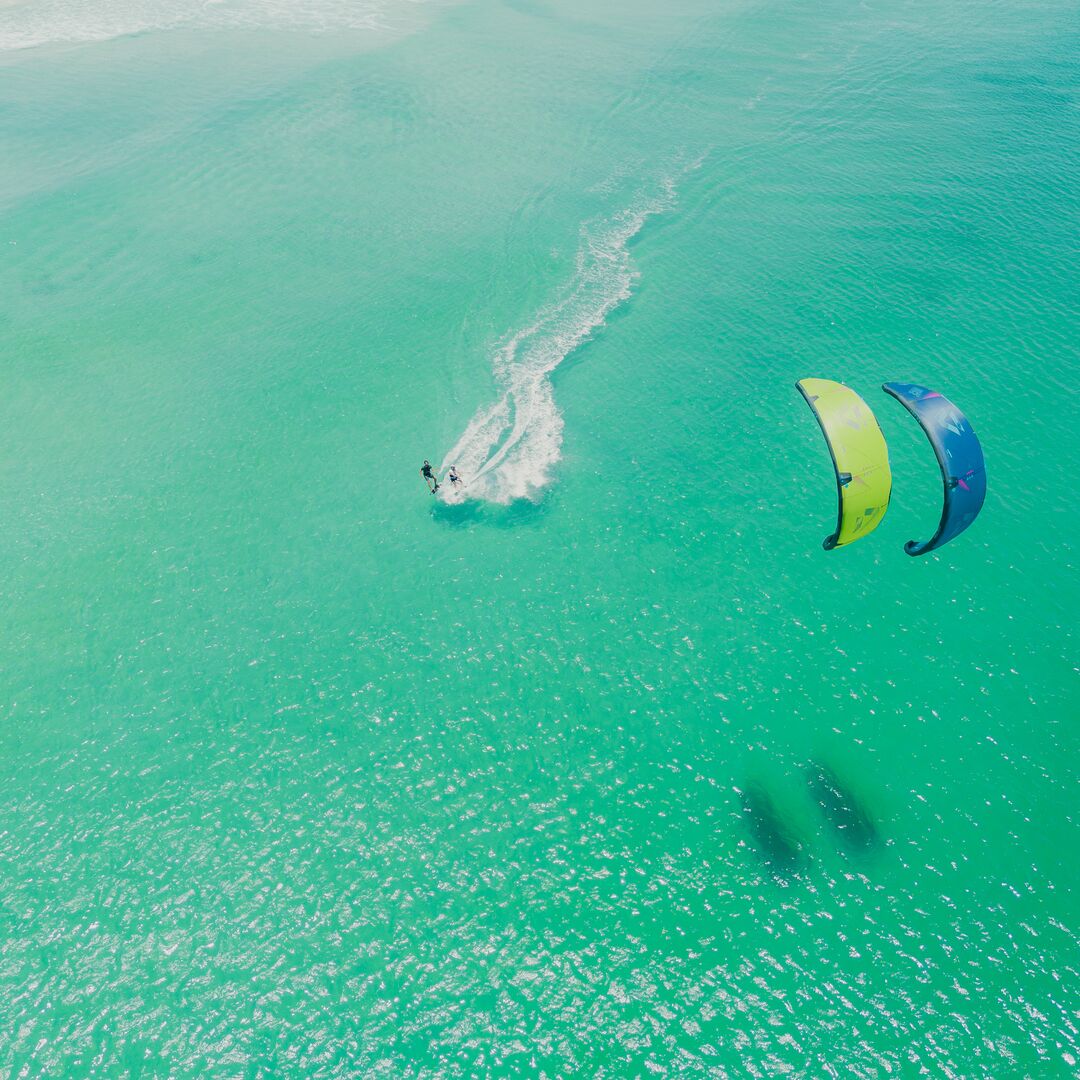 Deux riders naviguant côte à côte sur une mer calme sous un ciel ensoleillé, vue en contre-plongée, avec l’aile de kite DUOTONE JUICE 2025 bien visible en plein vol.