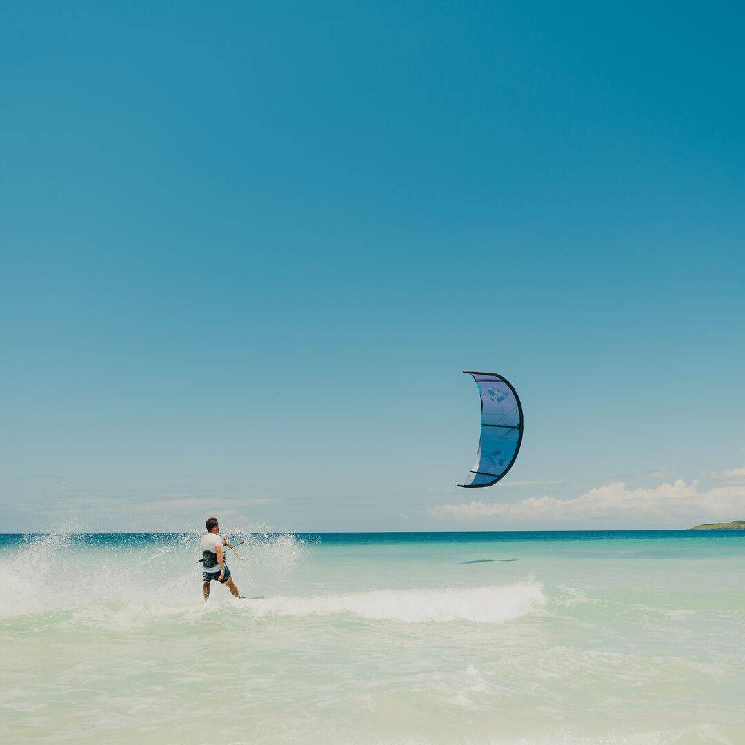 Un rider vu de dos naviguant debout sur une mer calme par temps ensoleillé avec l’aile de kite DUOTONE Juice 2025 en action.