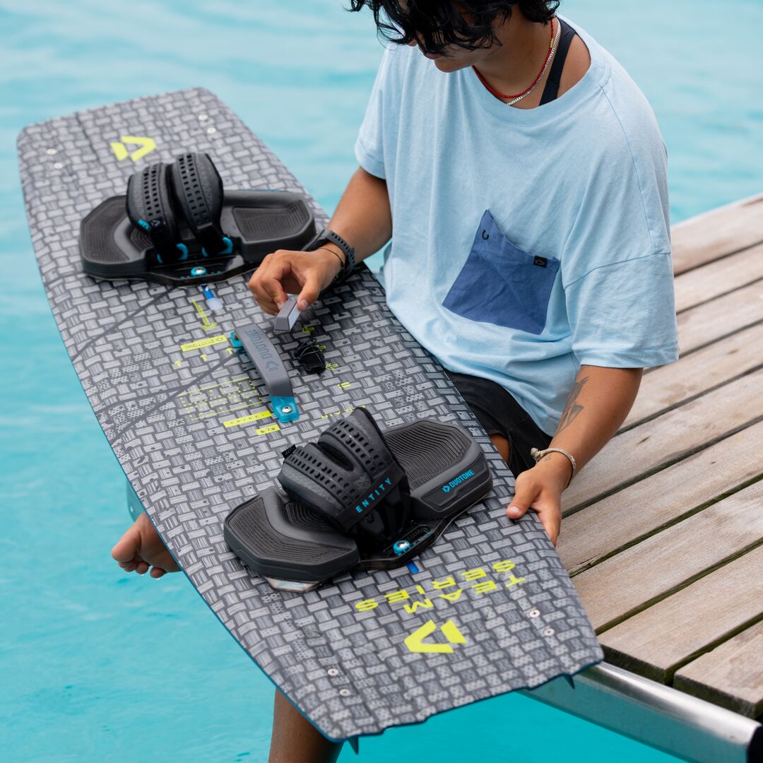 Rider ajustant les straps Duotone Entity Ergo 2025 sur une planche de kitesurf