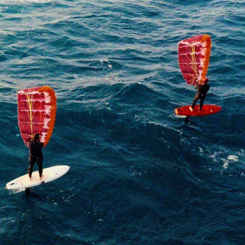Deux riders en wingfoil sur l’océan avec la F-ONE Frigate, aile rouge et orange gonflée, en navigation