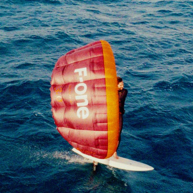 Navigation en wingfoil avec la F-ONE Frigate 3.0 m² rouge et orange, vue rapprochée sur l’aile gonflée