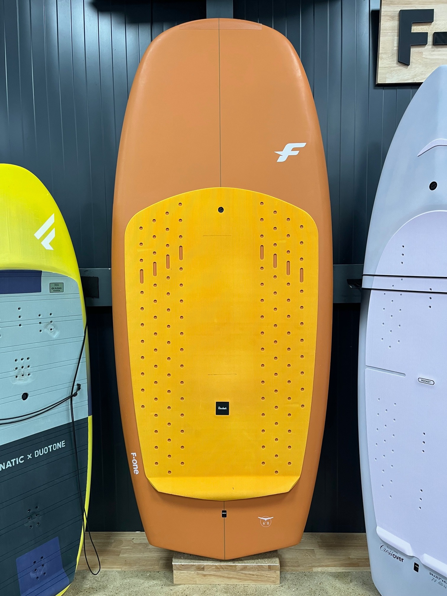 Planche wingfoil F-ONE Rocket Wing V2 6'0 120L occasion position verticale avec pad orange contre mur