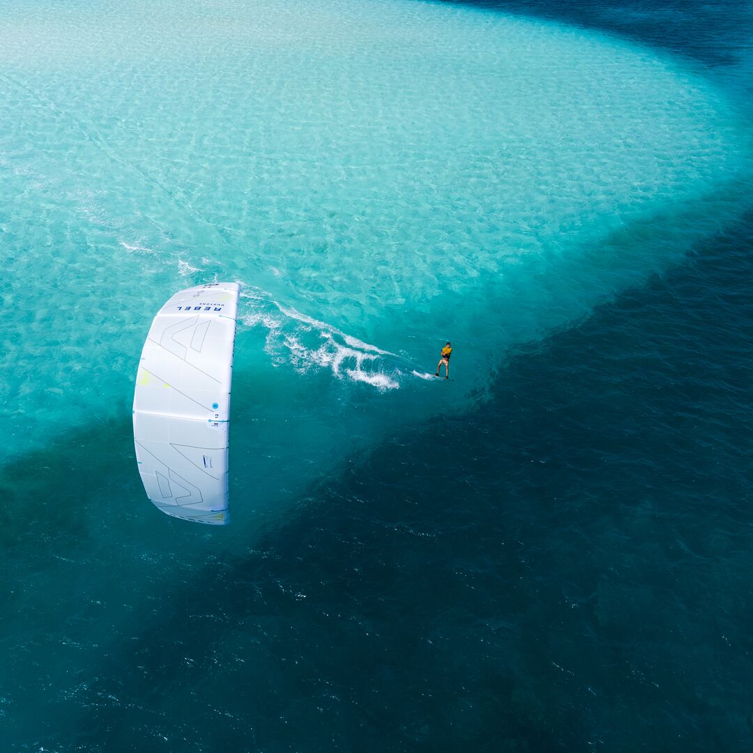 Rider pratiquant le kitesurf sur une mer peu profonde et calme, sous un temps ensoleillé, avec l'aile de kite Rebel SLS Concept Blue.