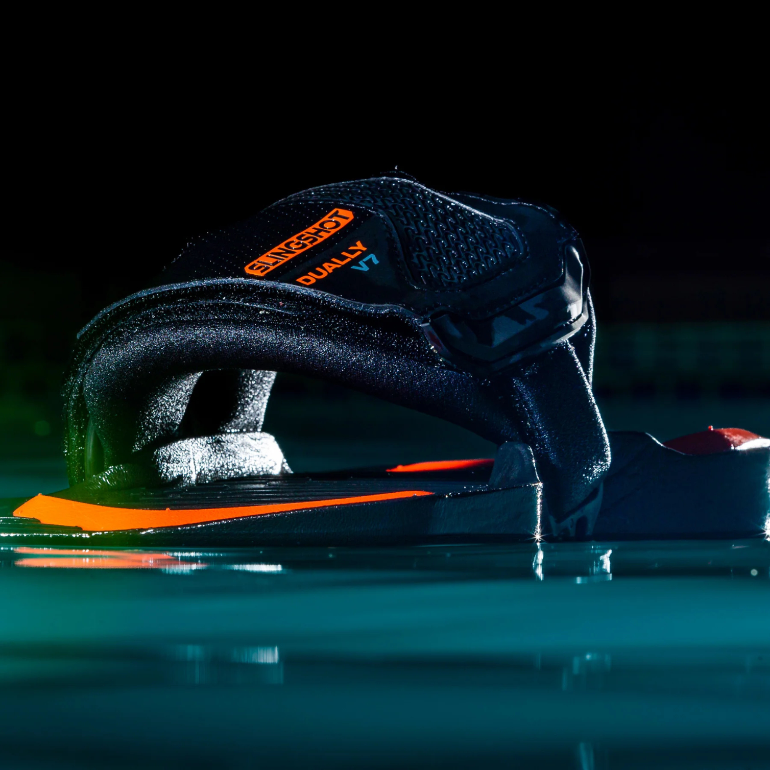 Les Pads Straps Slingshot Dually V7 2025 posés sur une surface d’eau, vue latérale en lumière basse avec détails orange et noirs