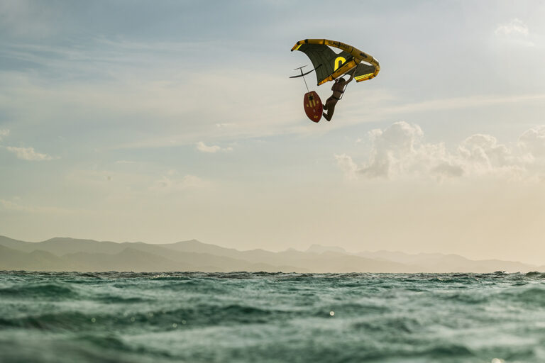 Rider en plein saut avec la Slingshot Flowcraft V2 et la wing NXT, démonstration de contrôle et de lift au-dessus de l’eau.
