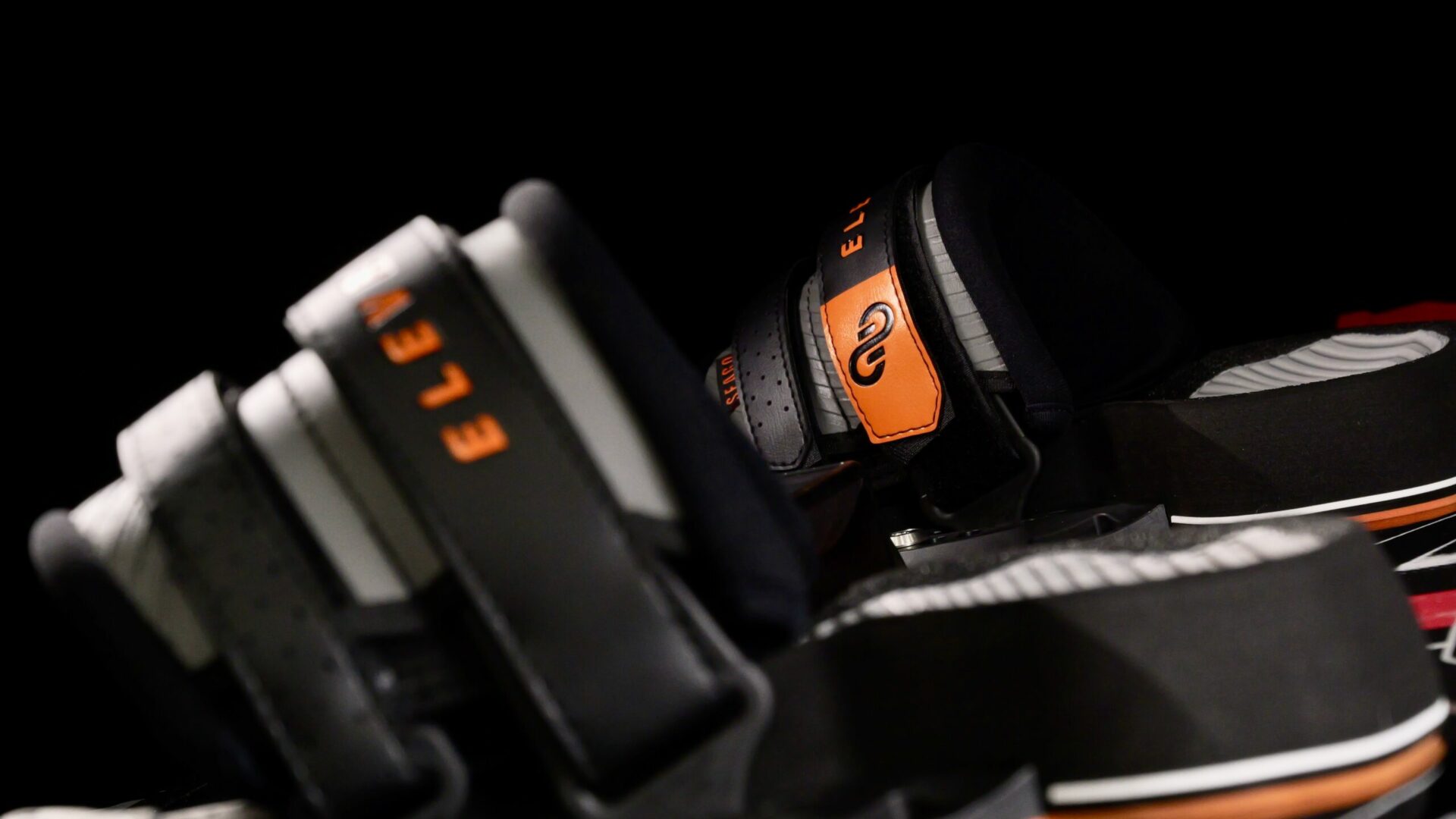 Logo SEAGO en blanc sur une surface orange, en arrière-plan des straps Eleveight Seago pour le kitesurf.