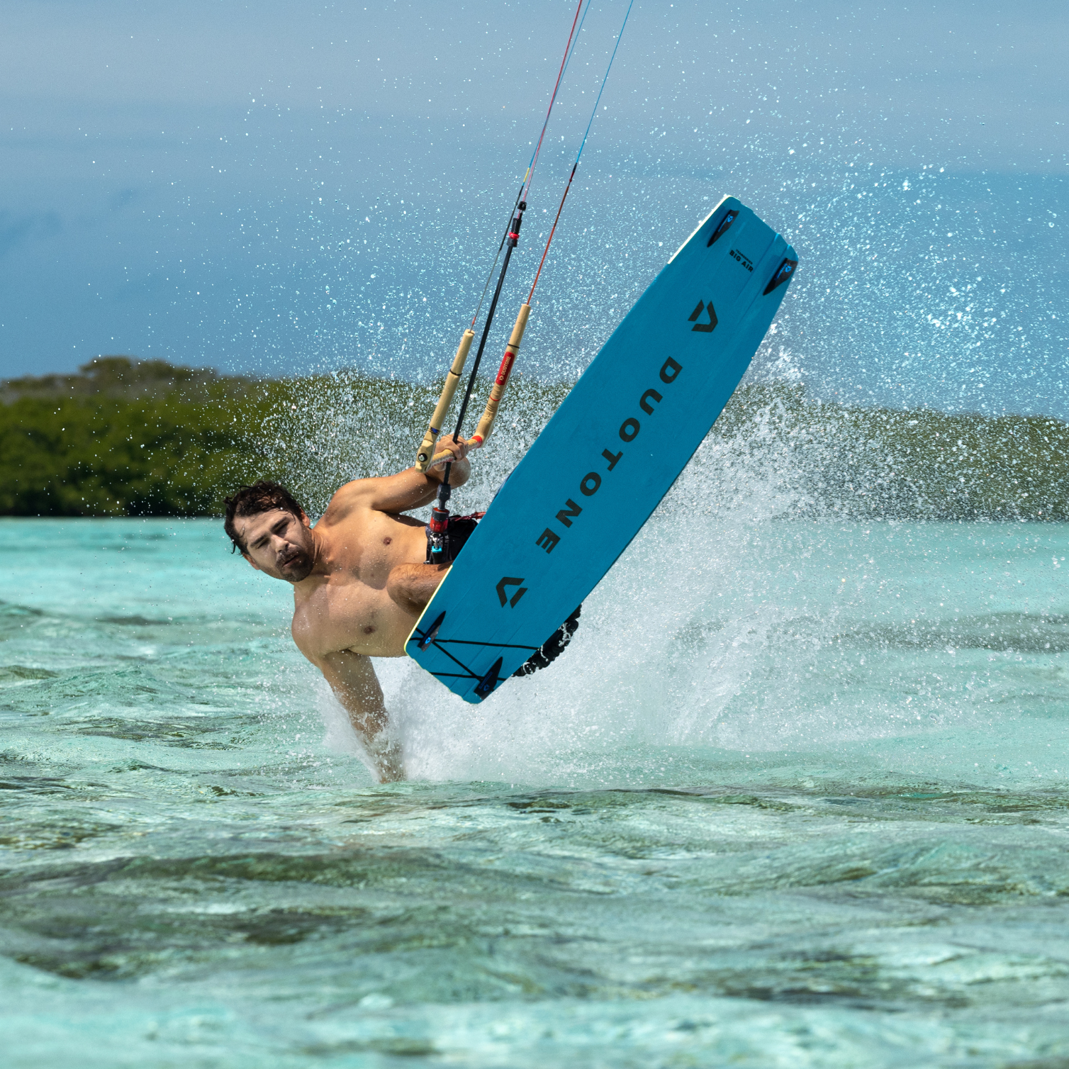 Kitesurfer réalisant une figure en surface avec la planche Duotone TS BIG AIR 2026, éclaboussures et maîtrise dans l’eau turquoise.